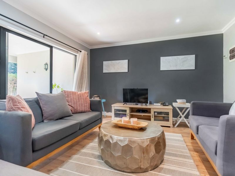 A well-maintained living room featuring laminate flooring, recessed downlights, and a large sliding glass door providing access to the outdoor area.