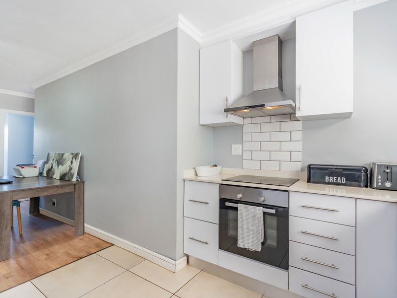 Modern kitchen featuring white cabinetry, stone countertops, subway tile backsplash, and integrated stainless steel appliances including an oven and extractor fan.