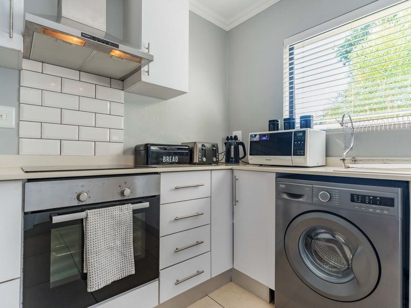 A compact, well-maintained kitchen featuring white cabinetry, subway tile backsplash, built-in oven, cooktop, and an integrated washing machine.