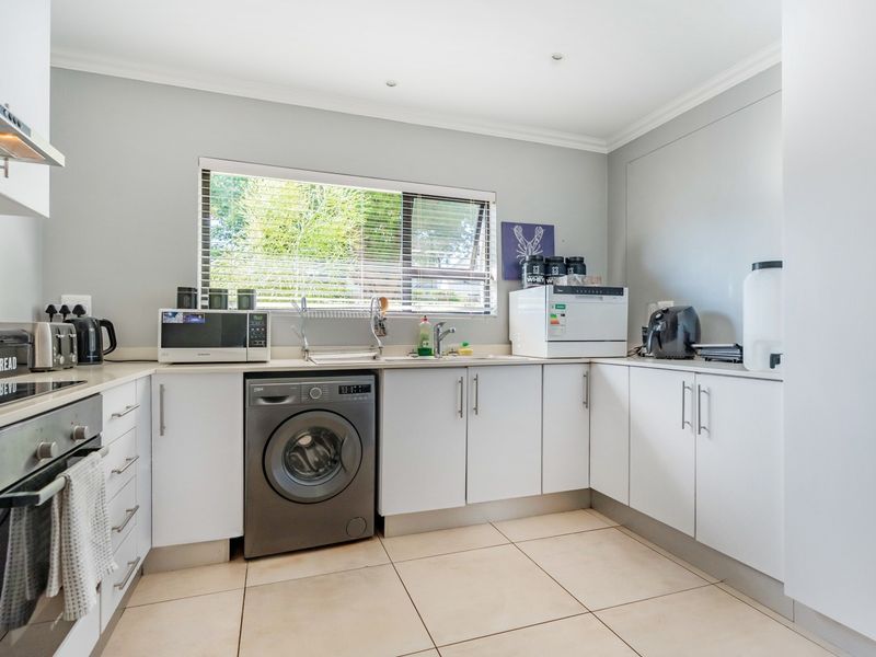 A functional kitchen featuring white cabinetry, tiled flooring, a built-in oven, extractor fan, and a stainless steel sink with a window view.
