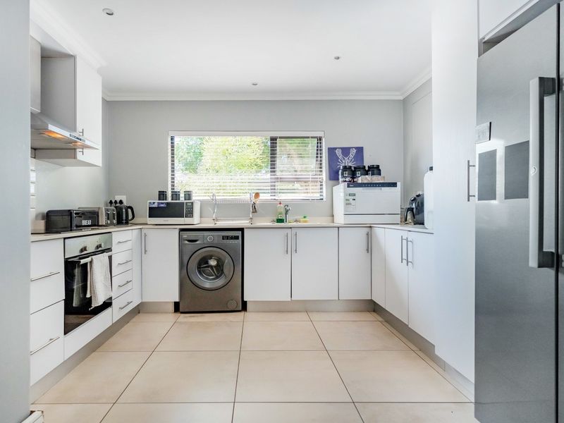 A clean and functional kitchen featuring white cabinetry, tiled flooring, integrated oven, extractor fan, and a stainless steel sink with a window view.