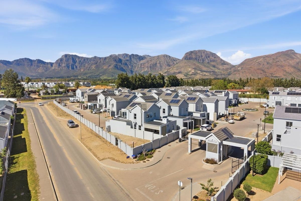 Aerial view of a modern residential estate featuring multiple houses with solar panels, a secure gated entrance, and mountain views.