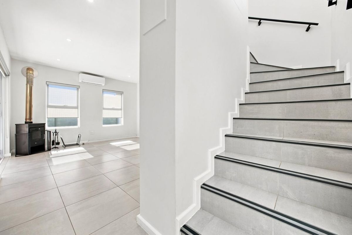 Bright open-plan living area featuring large format floor tiles, a modern wood-burning stove, and a tiled staircase with a sleek handrail.