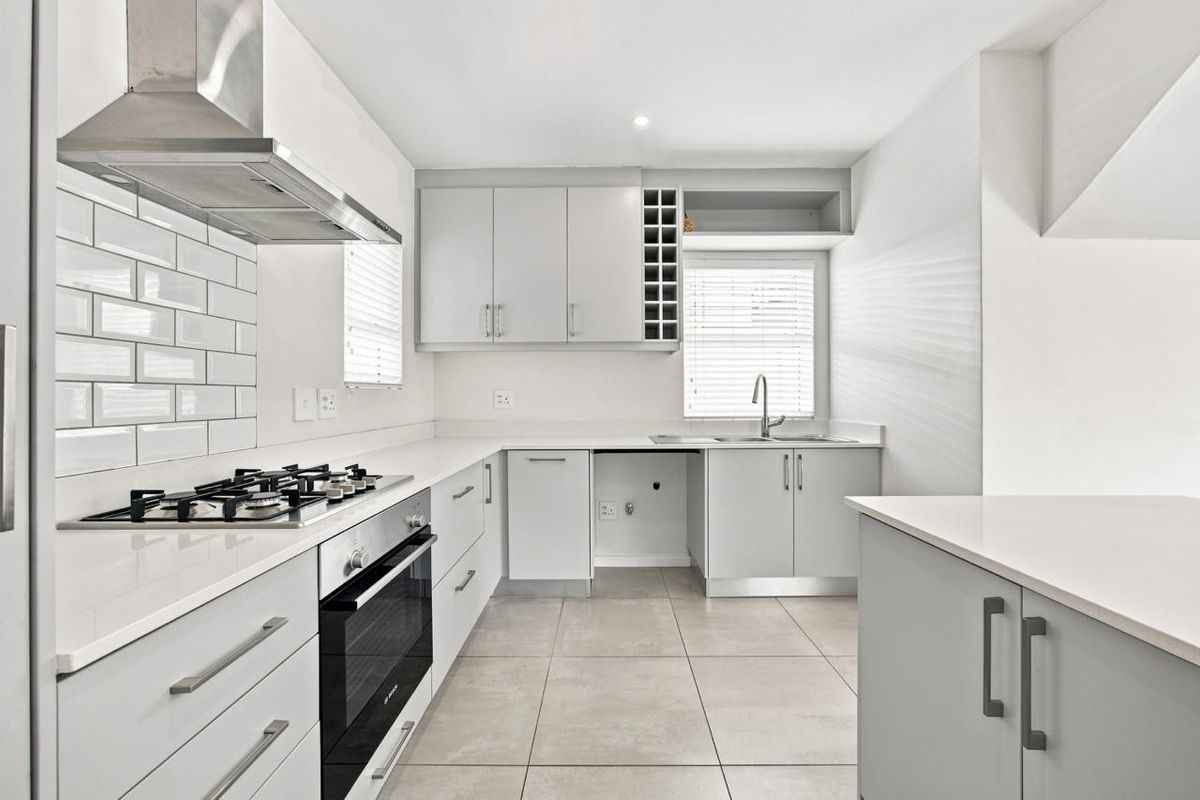 Modern kitchen featuring light grey cabinetry, quartz countertops, subway tile backsplash, gas hob, built-in oven, and tiled flooring in a clean, minimalist layout.