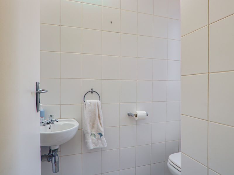 A compact guest bathroom featuring white ceramic wall tiles, a wall-mounted basin with chrome fixtures, and essential bathroom hardware.