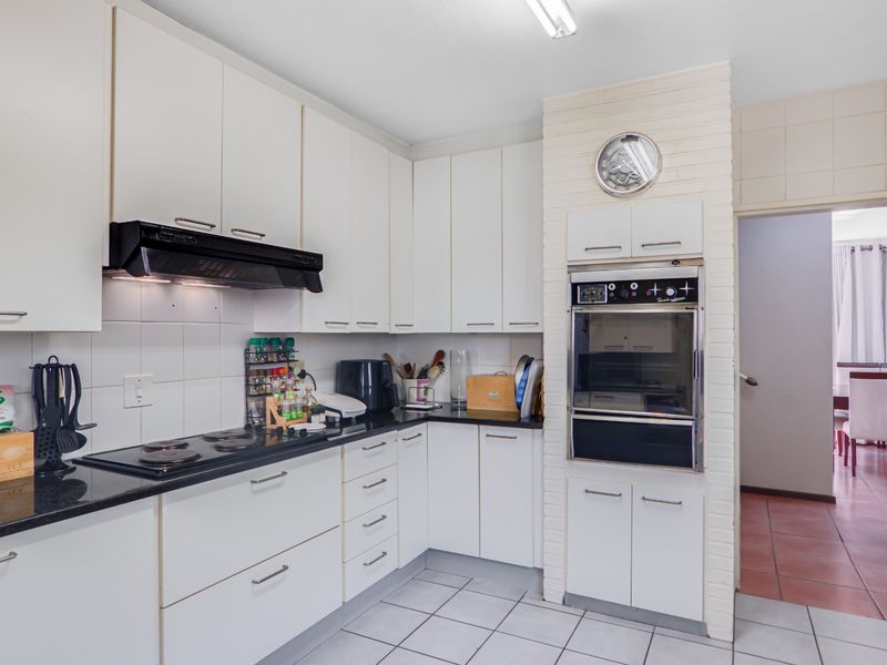 A functional kitchen featuring white cabinetry, black stone countertops, a built-in oven, and an electric hob with an integrated extractor fan.