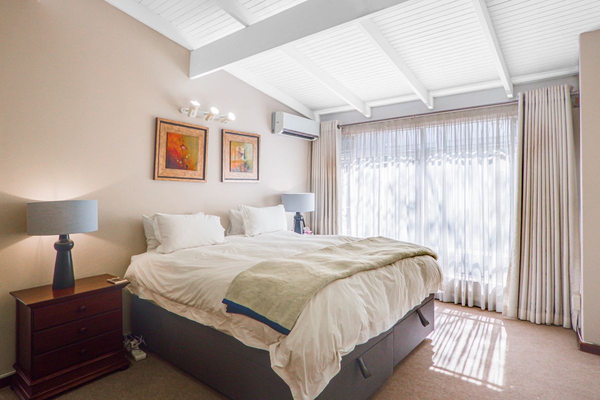 A well-lit bedroom featuring an exposed beam ceiling, split system air conditioning, and large sliding glass doors with floor-to-ceiling curtains.