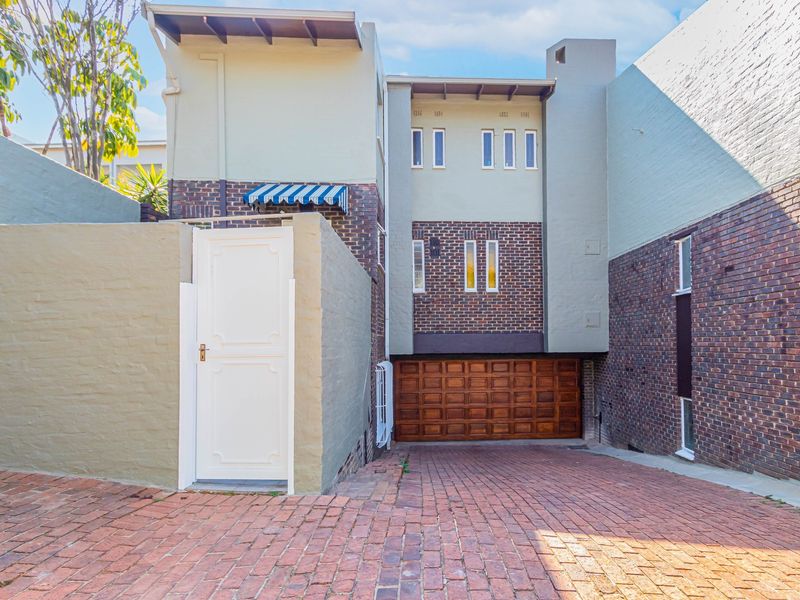 Front elevation of a townhouse featuring a brick driveway, a wooden garage door, and a pedestrian entrance gate.