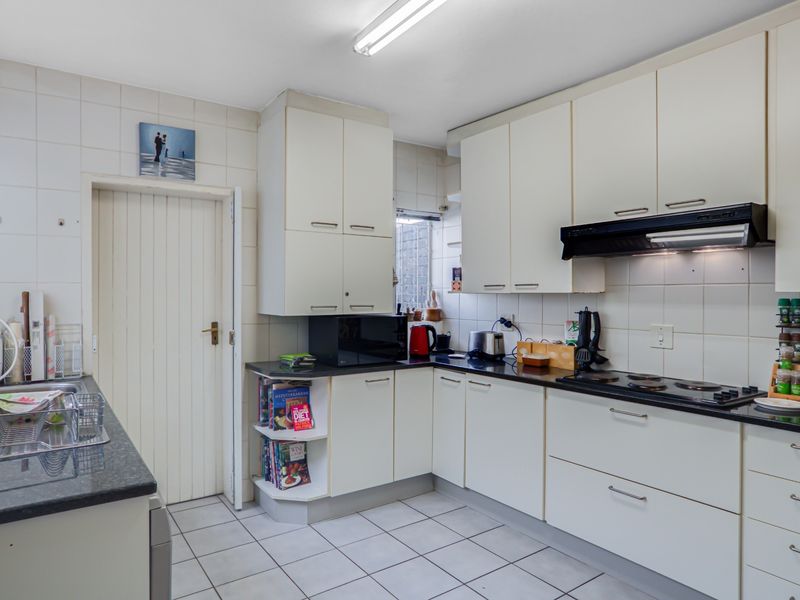 A functional kitchen featuring white cabinetry, dark laminate countertops, tiled backsplash, and ceramic flooring, equipped with a built-in electric hob and extractor fan.