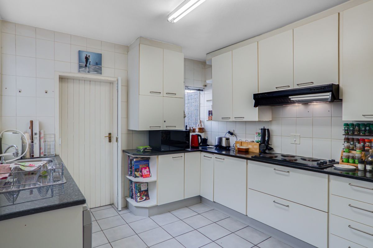 A functional kitchen featuring white cabinetry, dark laminate countertops, tiled backsplash, and ceramic flooring, equipped with a built-in electric hob and extractor fan.