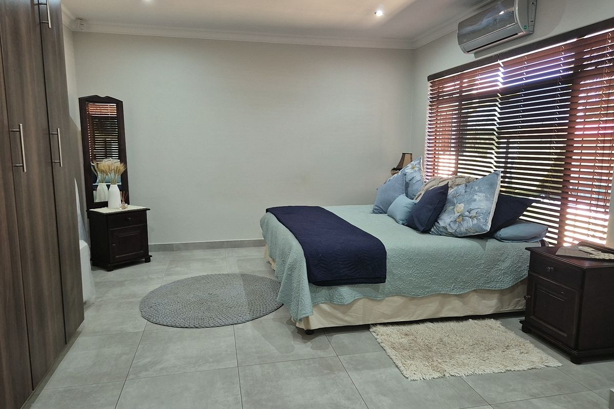 A well-maintained bedroom featuring large-format floor tiles, built-in cabinetry, a wall-mounted air conditioning unit, and adjustable venetian blinds.