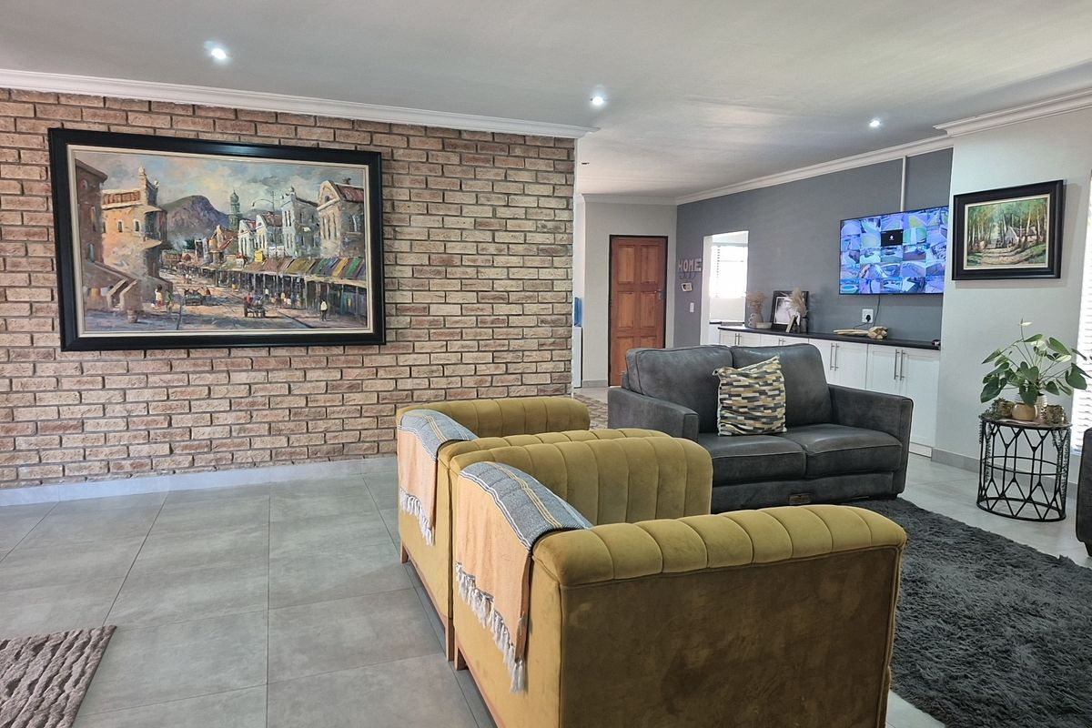 Spacious living area featuring a prominent exposed brick wall, modern tiled flooring, recessed lighting, and integrated cabinetry for storage.