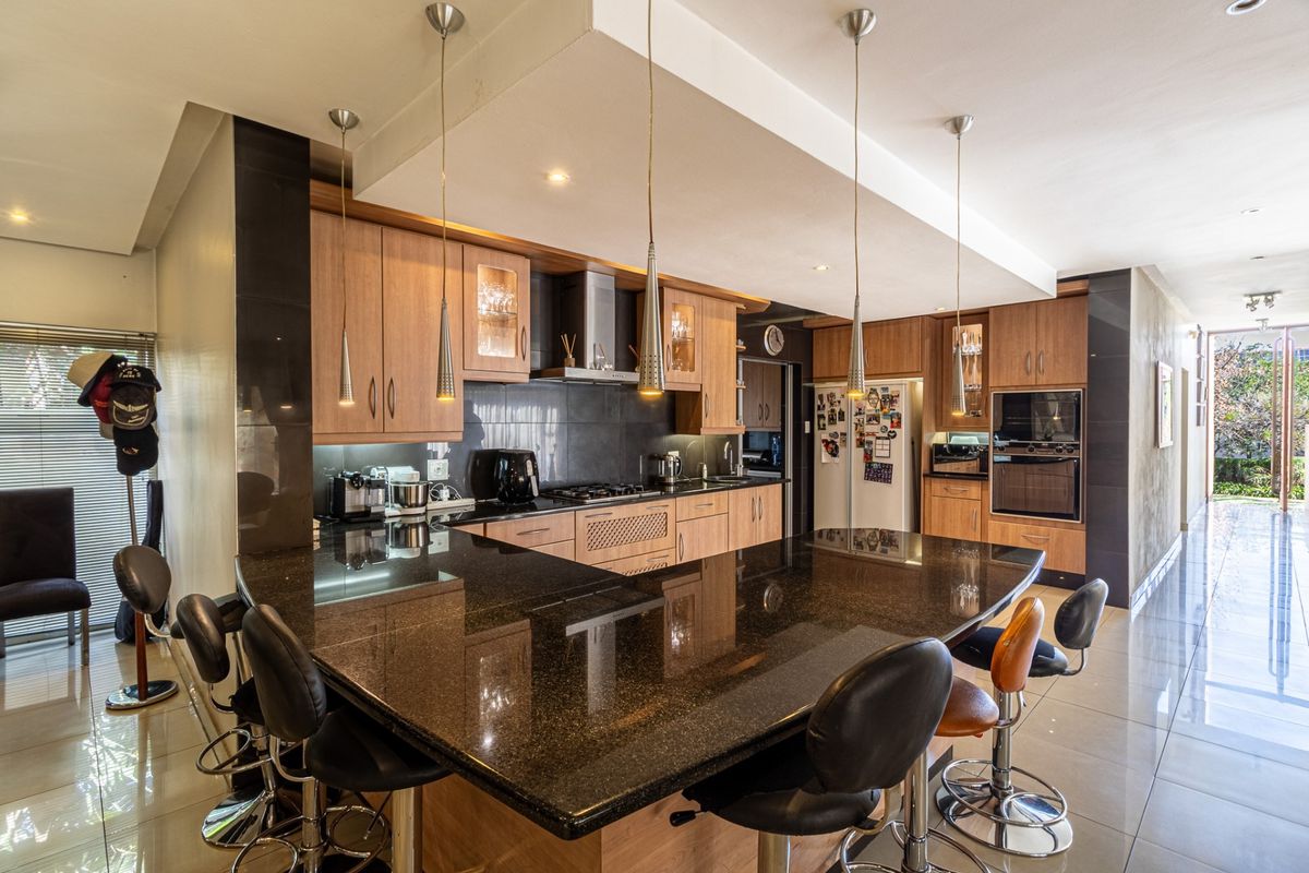 Modern kitchen featuring granite countertops, built-in cabinetry, integrated oven, and a breakfast bar with pendant lighting, flowing into an open-plan living area.