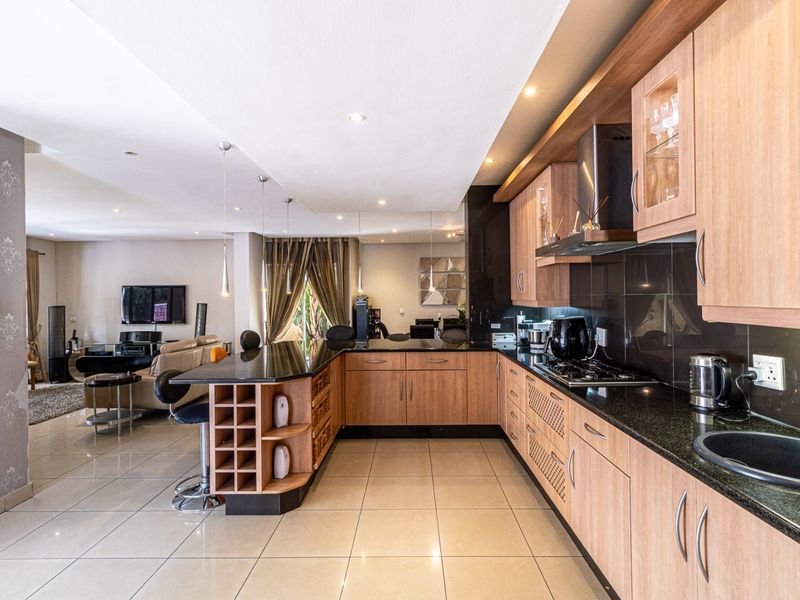 Open-plan kitchen featuring wood-finish cabinetry, granite countertops, gas hob, and integrated appliances, seamlessly flowing into the adjacent living area.