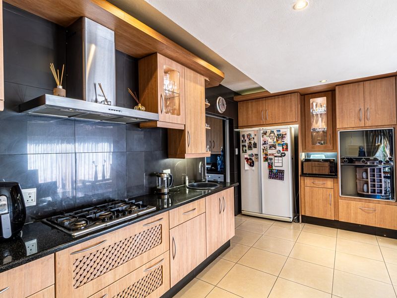 Modern kitchen featuring wood-finish cabinetry, granite countertops, gas hob, extractor fan, and integrated appliances with tiled flooring.