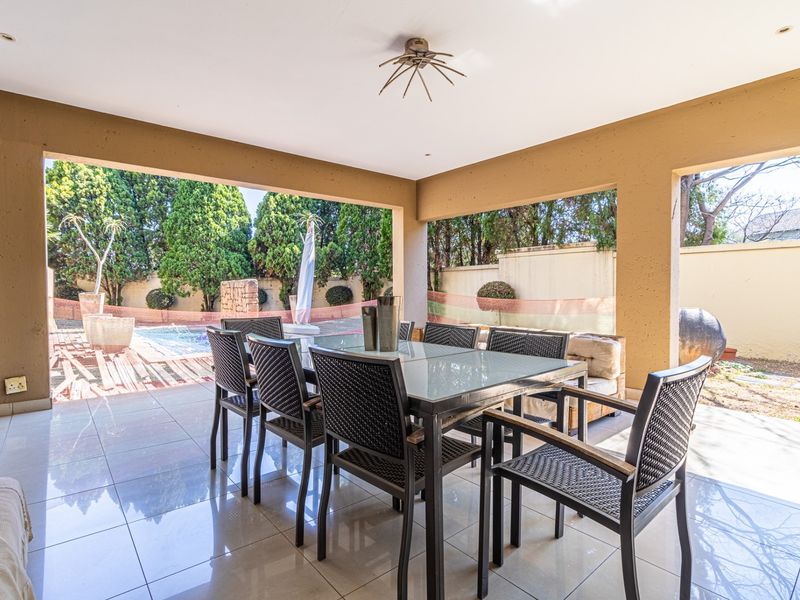 A spacious covered patio featuring tiled flooring and recessed lighting, providing a seamless transition to the outdoor pool and garden area.