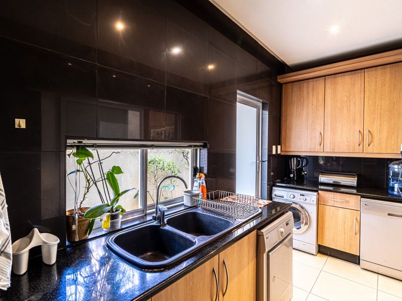 A functional scullery featuring dark granite countertops, double basin sink, built-in wooden cabinetry, and integrated laundry appliances.