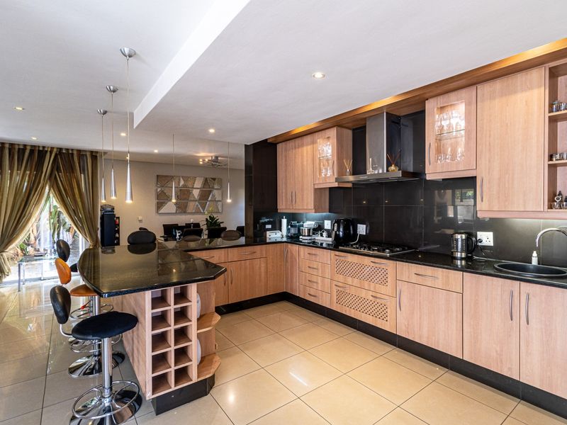 Modern kitchen featuring light wood cabinetry, granite countertops, integrated appliances, and a breakfast bar, seamlessly flowing into the adjacent dining area.