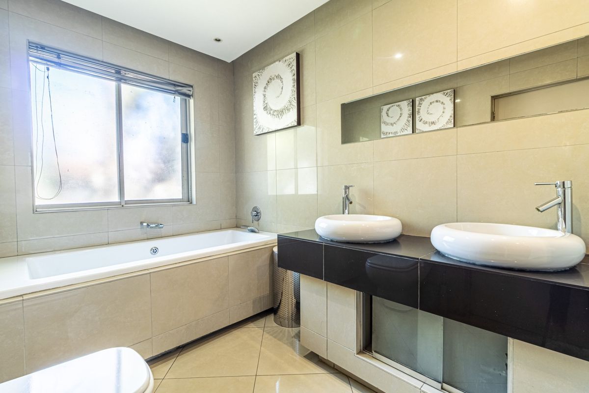 Modern bathroom featuring a built-in bathtub, double vanity with vessel sinks, chrome fixtures, and neutral wall and floor tiling.