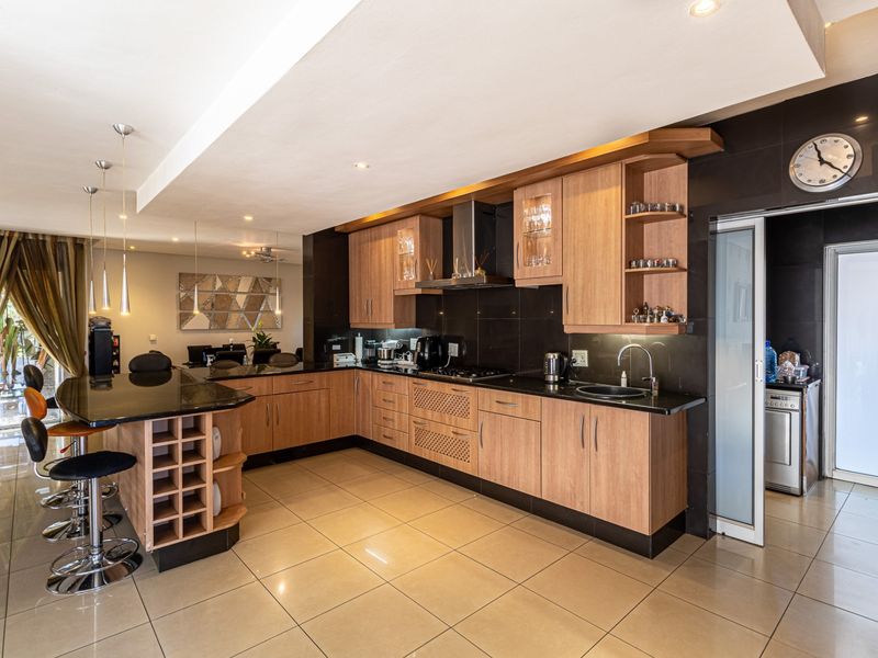 Spacious open-plan kitchen featuring wood-finish cabinetry, granite countertops, a breakfast bar, and integrated appliances, seamlessly flowing into the adjacent living and dining area.