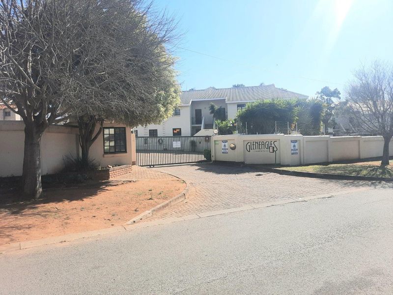 Front entrance view of Gleneagles apartment complex featuring a secure gated access point, perimeter wall with electric fencing, and paved driveway.