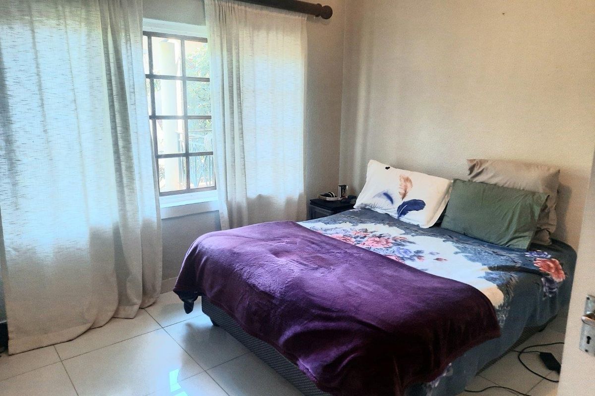 A bedroom featuring tiled flooring and a grid-pattern window with natural light, providing a functional and neutral space.