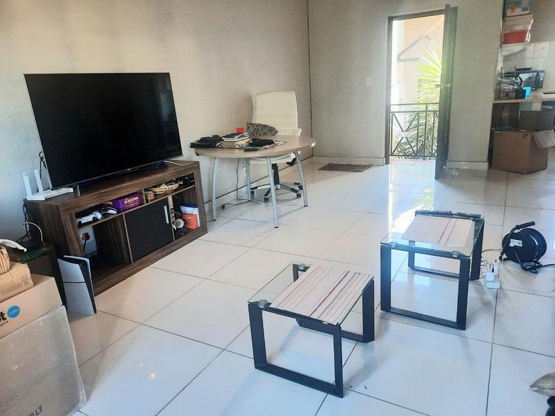 A living room area featuring white tiled flooring and direct access to an outdoor balcony through a glass-paneled door.
