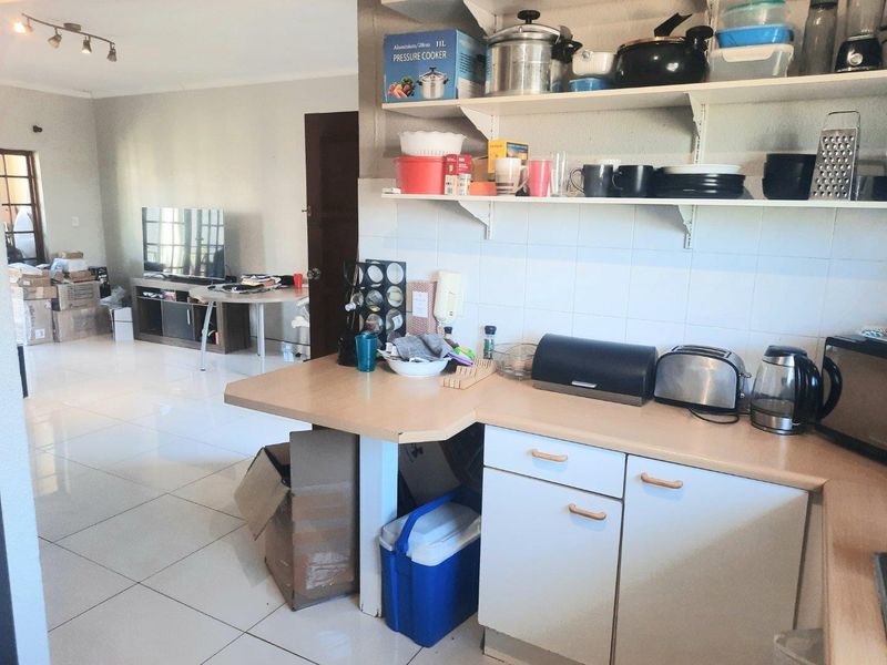 Open-plan living and kitchen area featuring tiled flooring, laminate countertops, and wall-mounted shelving, offering a functional layout for modern apartment living.