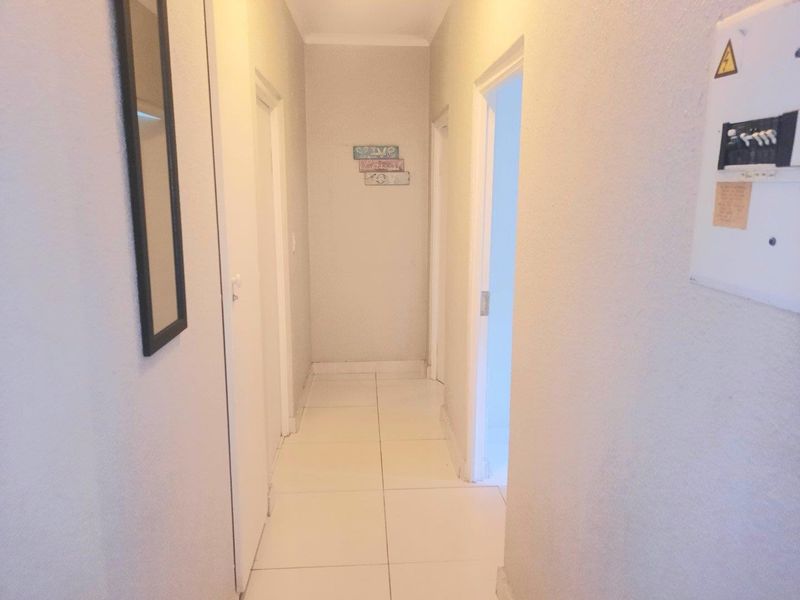 A clean, neutral-toned hallway featuring tiled flooring and a wall-mounted electrical distribution board, providing access to multiple rooms within the apartment.