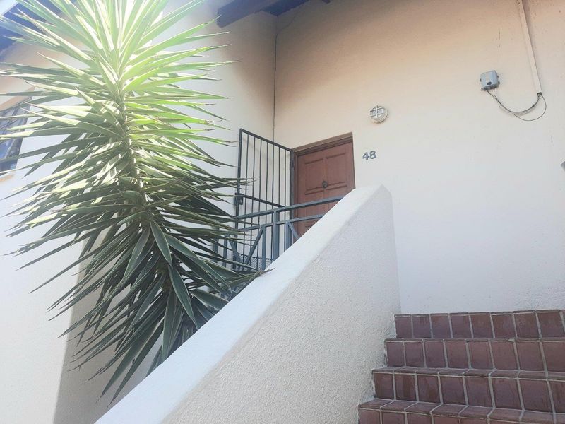 Front entrance of the apartment featuring a tiled staircase, security gate, and exterior wall lighting.