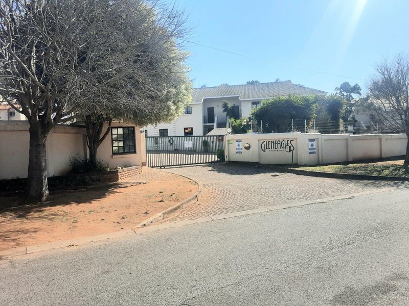 Front entrance view of Gleneagles apartment complex featuring a paved driveway, secure gated access, and perimeter wall with electric fencing.