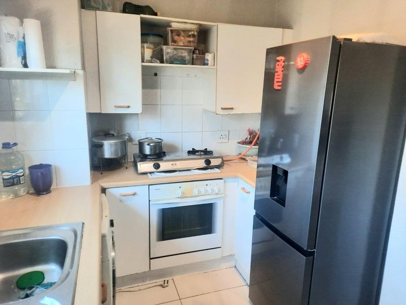Compact kitchen featuring white built-in cabinetry, laminate countertops, a stainless steel sink, and a built-in oven with a gas hob.
