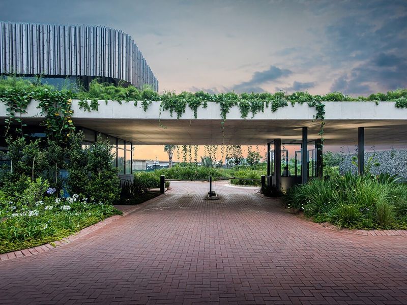 Modern entrance gatehouse featuring a concrete canopy, lush vertical landscaping, and a brick-paved driveway leading into the property.