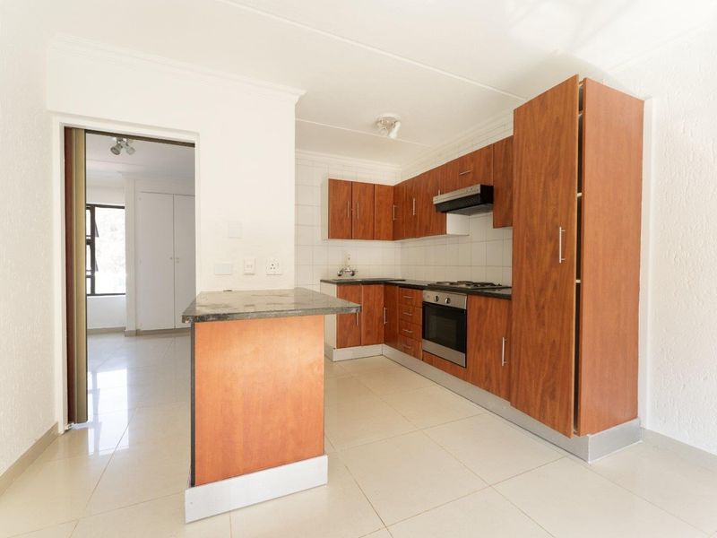 A clean, functional kitchen featuring wood-finish cabinetry, granite countertops, built-in oven, gas hob, and a convenient breakfast nook with tiled flooring throughout.