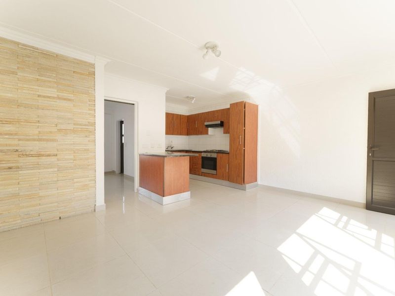 Open-plan living area featuring a kitchen with built-in cabinetry, oven, and hob, complemented by a stone feature wall and neutral tiled flooring.