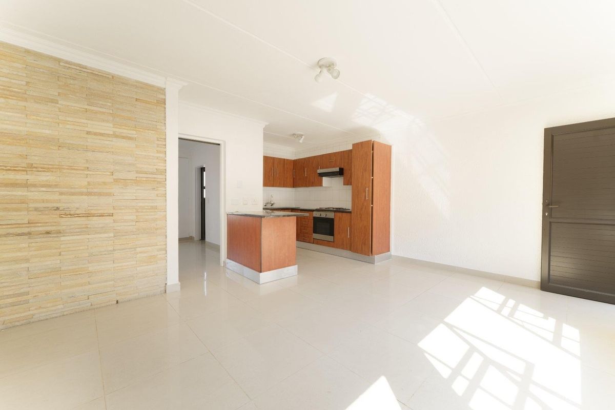Open-plan living area featuring a kitchen with built-in cabinetry, oven, and hob, complemented by a stone feature wall and neutral tiled flooring.