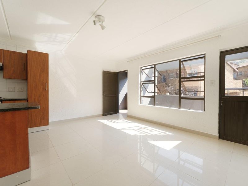 Bright open-plan living area featuring tiled floors, built-in kitchen cabinetry with granite countertops, and direct access to an outdoor space.