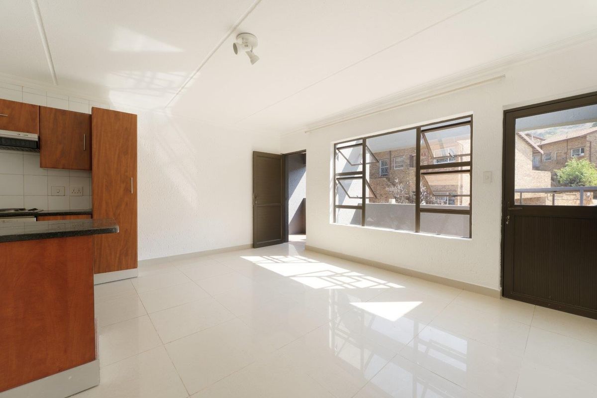 Bright open-plan living area featuring tiled floors, built-in kitchen cabinetry with granite countertops, and direct access to an outdoor space.