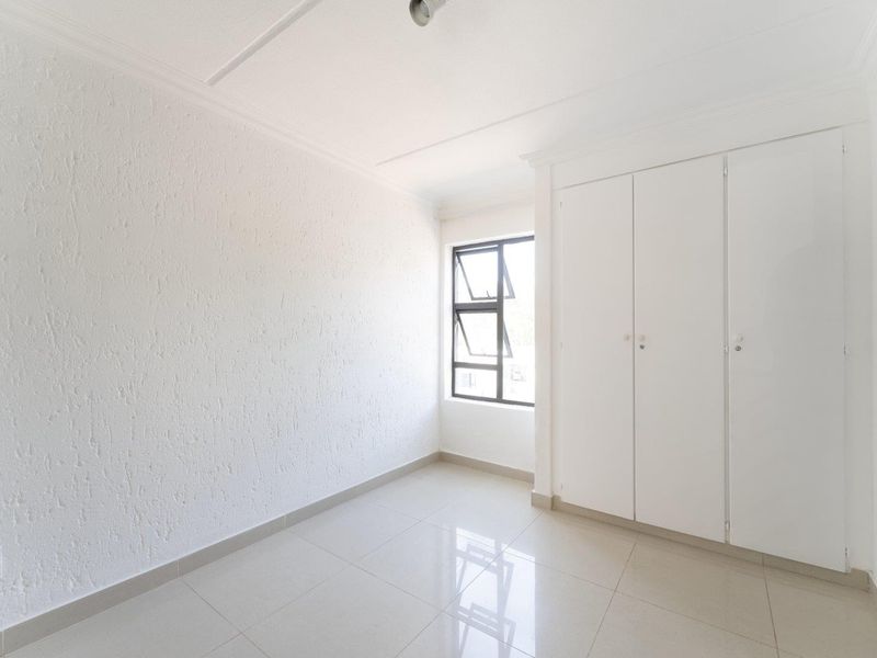 A bright, empty bedroom featuring neutral tiled flooring, white walls, and built-in cupboards, offering a clean and versatile space.
