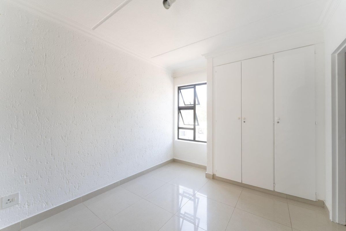 A bright, empty bedroom featuring neutral tiled flooring, white walls, and built-in cupboards, offering a clean and versatile space.
