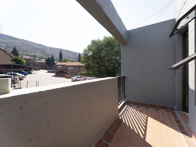 A private balcony featuring terracotta tiling, a metal balustrade, and a concrete parapet wall, offering views of the complex and surrounding landscape.