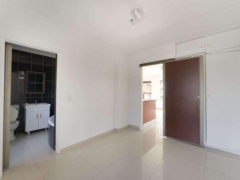 An empty bedroom featuring tiled flooring, built-in cupboards, and direct access to an en-suite bathroom.