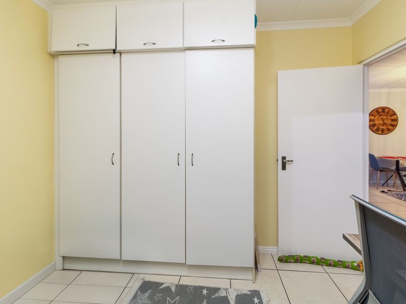 A bedroom featuring white built-in cupboards with overhead storage and tiled flooring, providing functional storage space.