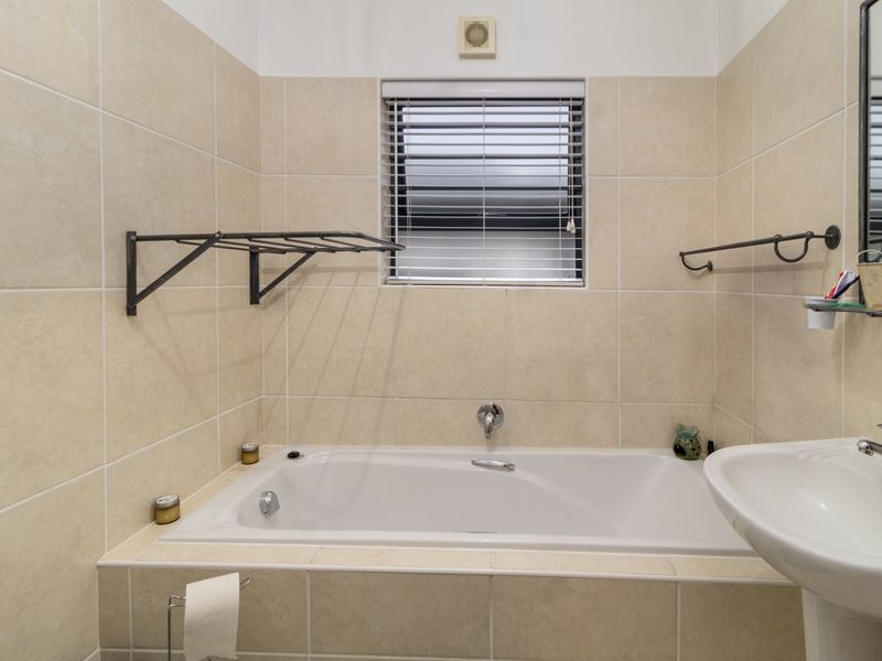 A functional bathroom featuring a built-in bathtub, pedestal basin, and neutral wall tiling, complemented by a window with a venetian blind.
