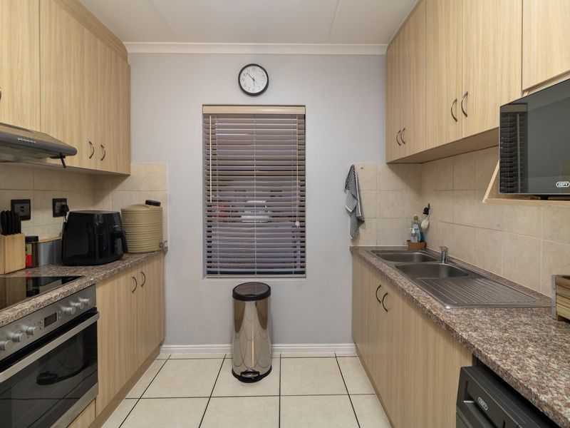 A functional galley-style kitchen featuring light wood-finish cabinetry, laminate countertops, a built-in oven with hob, and tiled flooring.