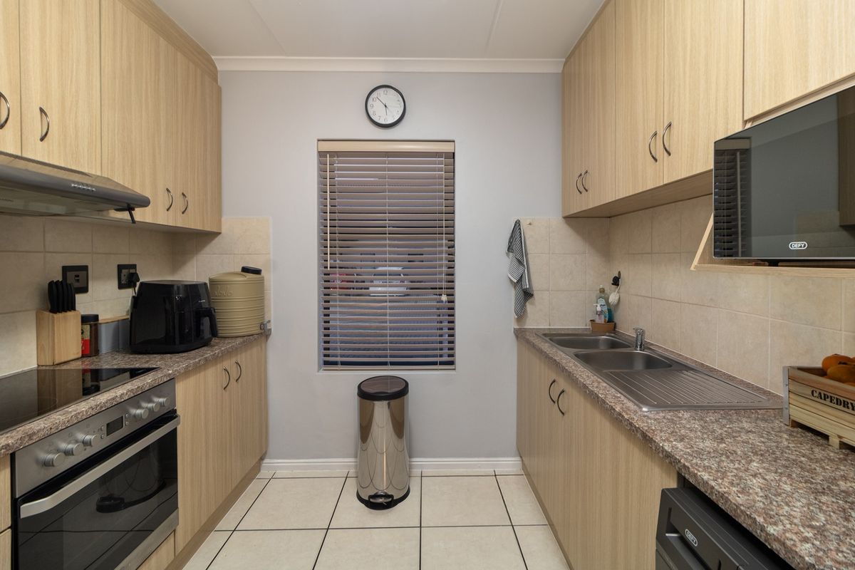 A functional galley-style kitchen featuring light wood-finish cabinetry, laminate countertops, a built-in oven with hob, and tiled flooring.