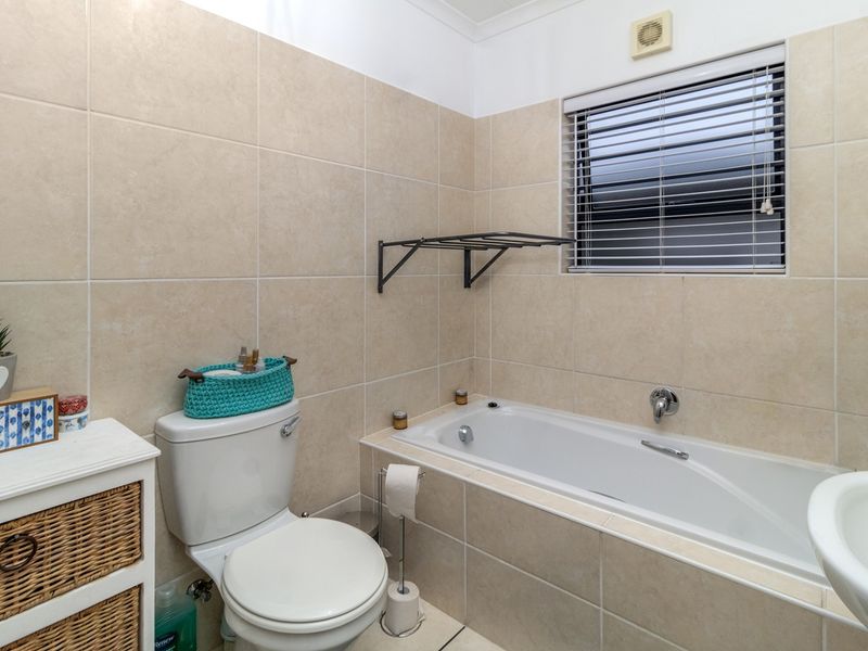 A functional bathroom featuring a built-in bathtub, toilet, and neutral ceramic wall tiling with an integrated extractor fan.