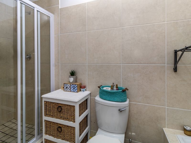 A functional bathroom featuring a glass shower enclosure, a standard toilet, and neutral wall tiling throughout.