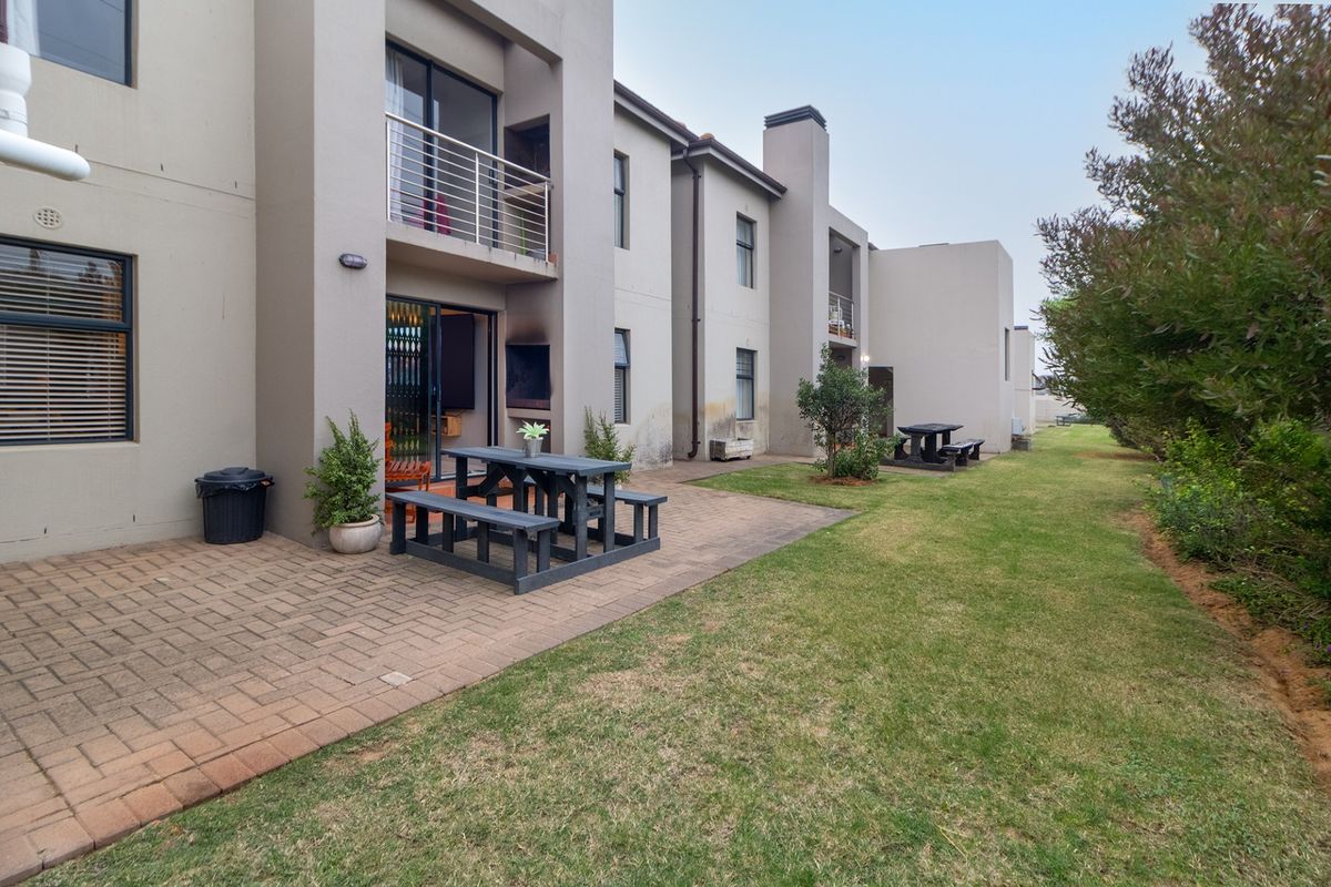 Rear view of the apartment complex featuring a paved patio area, ground floor access via sliding doors, and upper-level balconies with metal railings.