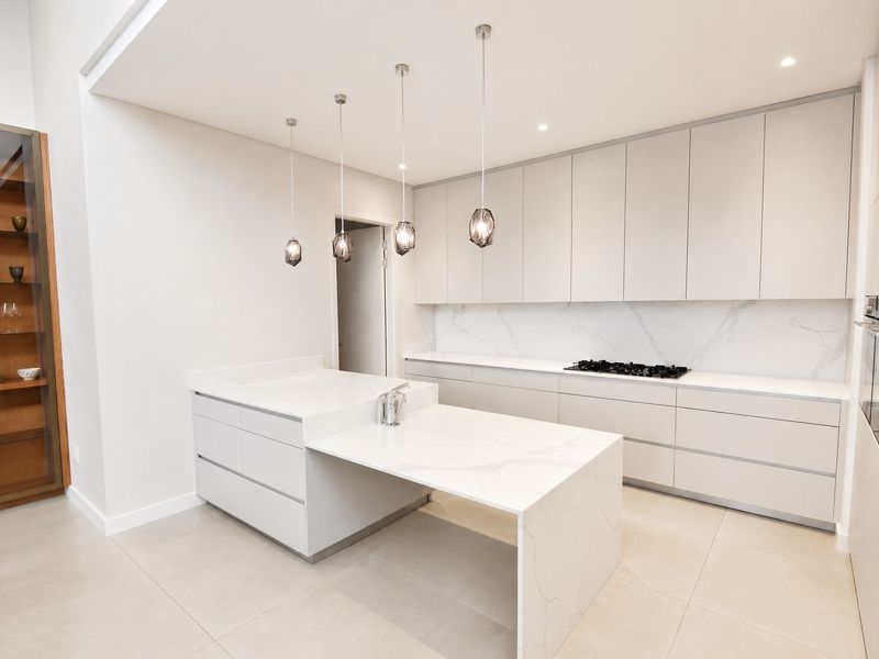Modern, minimalist kitchen featuring sleek handleless cabinetry, a stone-topped island, integrated gas hob, and high-end finishes throughout.